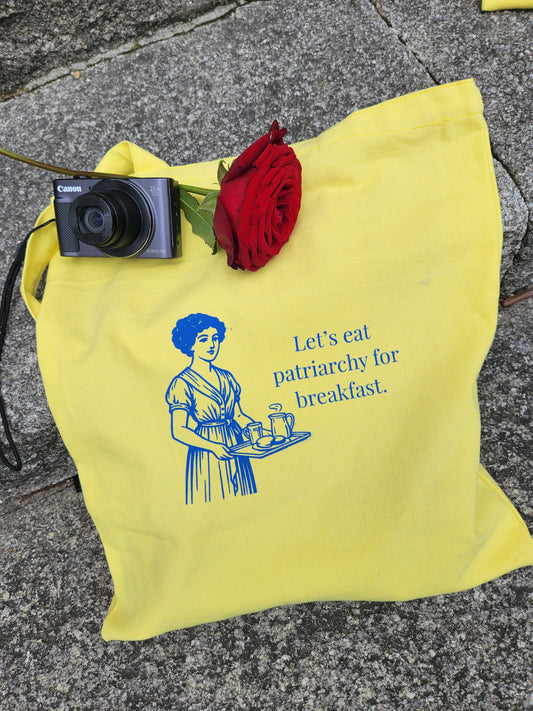 Close-up of blue feminist print on yellow canvas tote with a funny patriarchy joke by tantrm