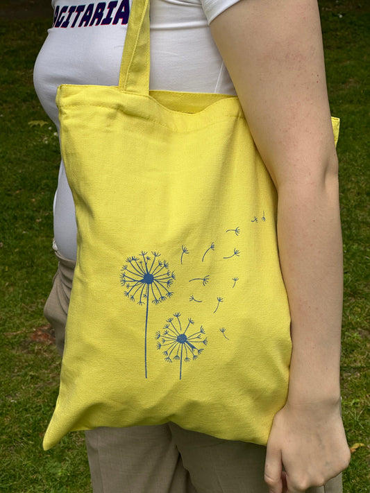 Close up of yellow canvas tote bag with blue dandelion print, designed by Tantrm