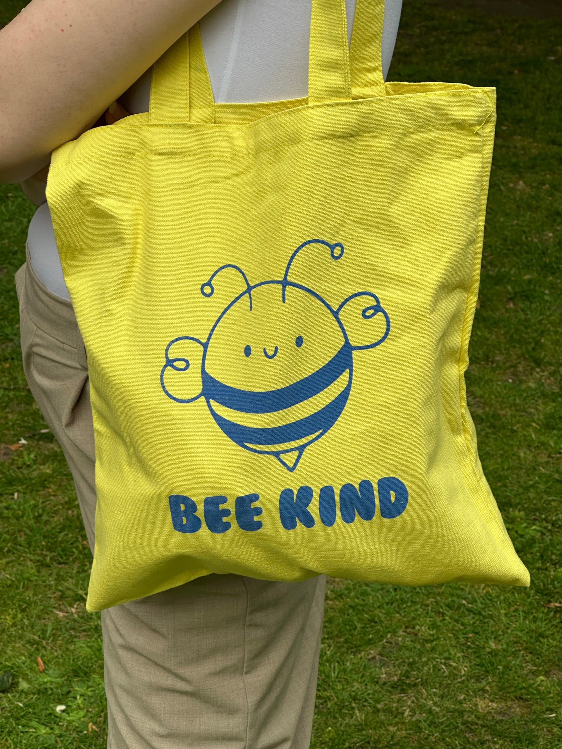 Yellow canvas tote bag with cute smiling bee and “BEE KIND” text, designed by Tantrm